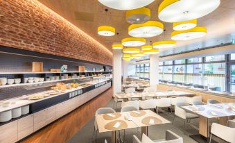 a modern cafeteria with a long dining table and several chairs , as well as several potted plants at Hey Lou Hotel Frankfurt Airport