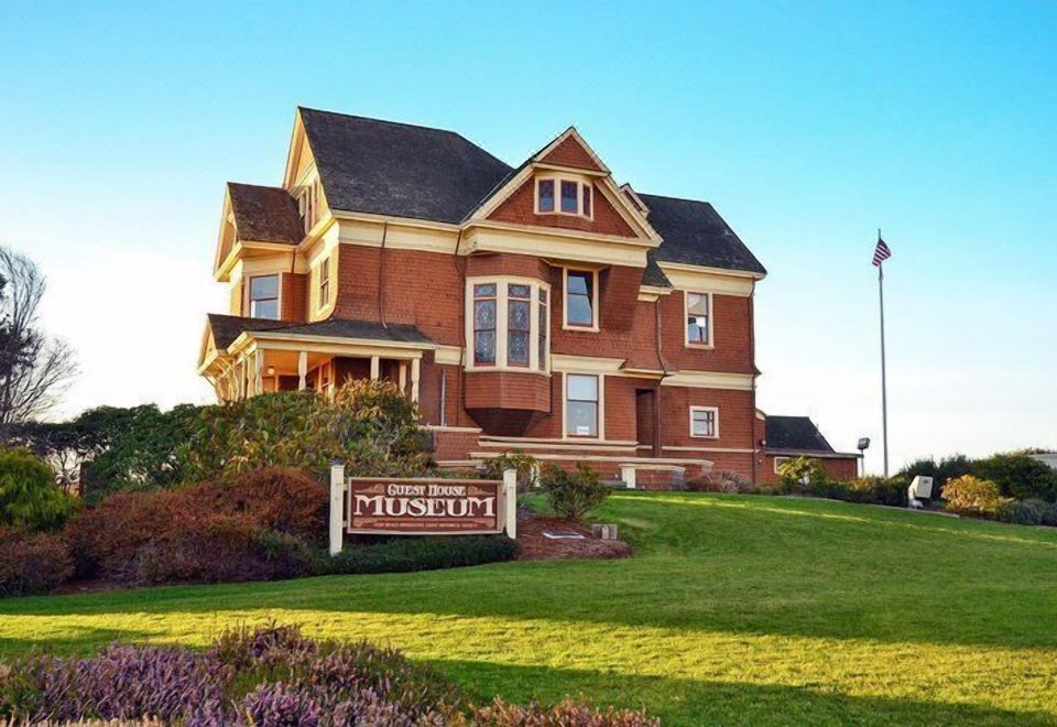 "a large brick building with a sign that reads "" brick house museum "" is surrounded by a grassy yard and a flagpole" at Seabird Lodge Fort Bragg