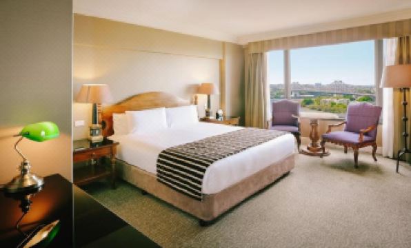 a large bed with a striped blanket is in a room with a chair , lamps , and a window at Stamford Plaza Brisbane
