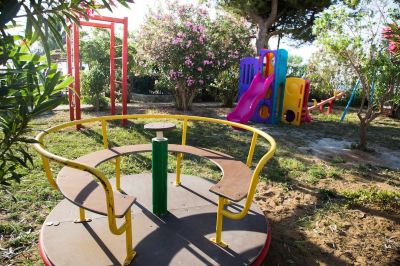 a colorful playground with a swing , slide , and other play equipment surrounded by trees and flowers at Hotel Summery