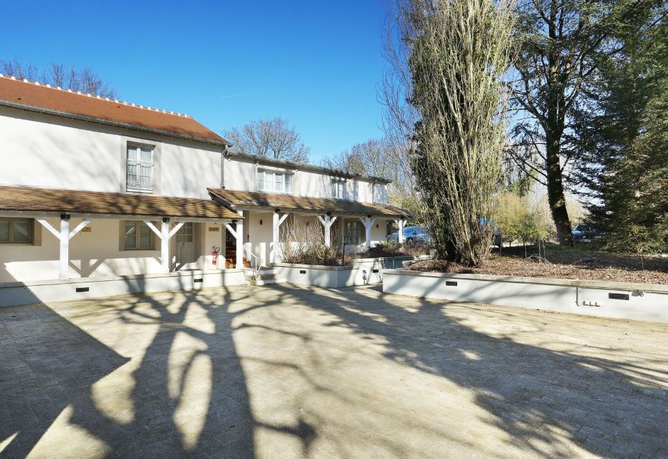 a large white building with a red roof is surrounded by trees and a small courtyard at Hob le Cheval Blanc