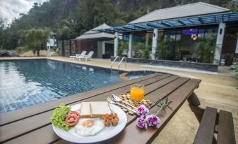 a table with a plate of food , a glass of orange juice , and flowers by a pool at Phuphayot Resort