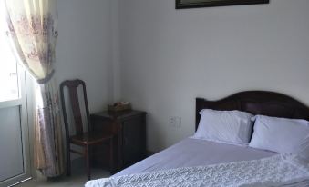 a cozy bedroom with a white bed , curtains , and a small table near the window at Hotel Nguyen Ngoc