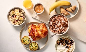 a variety of breakfast foods , including pancakes and granola , are displayed on plates and bowls at Delta Hotels by Marriott Milwaukee Northwest