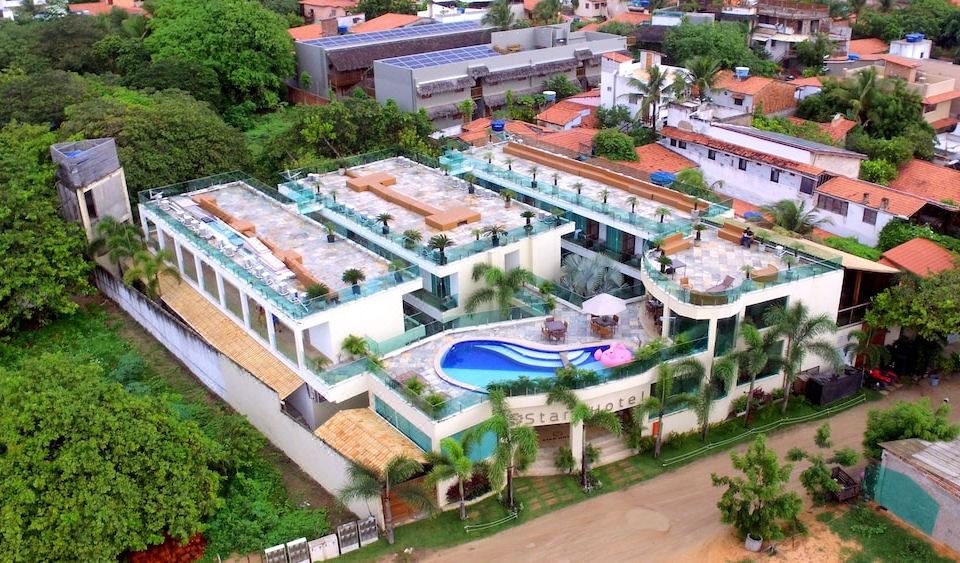 aerial view of a large , multi - level building with a swimming pool in the middle surrounded by palm trees and buildings at Star Hotel