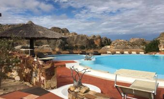 a large swimming pool with a thatched roof hut and rock formations in the background at Isalo Rock Lodge