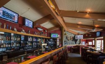 a well - lit bar with multiple tvs mounted on the wall and a counter area filled with bottles of alcohol at Westmark Sitka