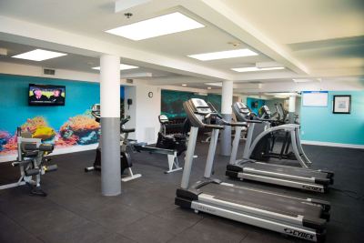 a well - equipped gym with various exercise equipment , including treadmills and weight machines , under a large mural at Wyndham Reef Resort Grand Cayman