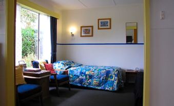 a bedroom with a bed , desk , and chair is shown next to a window and wall at King Island Accommodation Cottages
