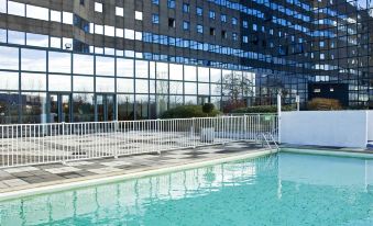 an outdoor swimming pool surrounded by a hotel , with a view of the surrounding buildings at Novotel Marne-la-Vallée Noisy-Le-Grand