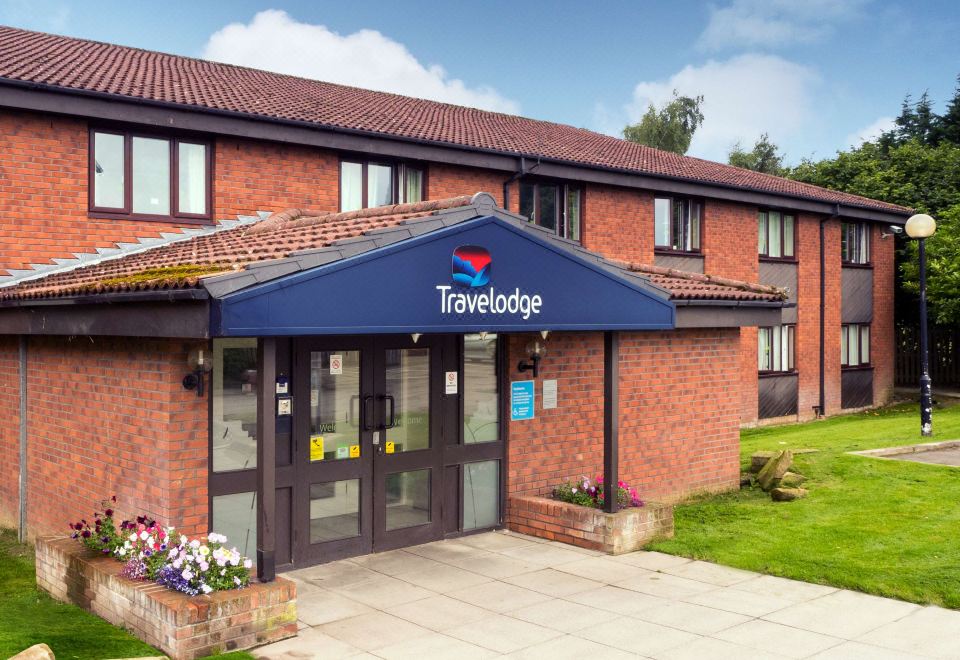 a travelodge hotel with its blue sign and flowers in front of the building , under a clear blue sky at Travelodge Scotch Corner Skeeby