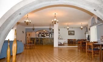 a large room with wooden floors and arches , containing several dining tables and chairs , as well as chandeliers hanging from the ceiling at Anamar Patmos