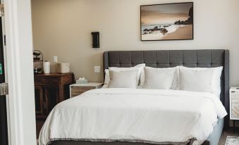 a large bed with white sheets and a gray headboard is in a room with a framed picture on the wall at Riverside Suites