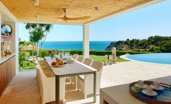 a dining table with a view of the ocean , surrounded by white chairs and a couch at Vila Vita Parc