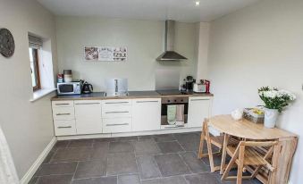 a modern kitchen with white cabinets , a dining area , and a wooden table with chairs at Hillcroft Accommodation