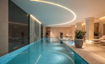 a modern indoor swimming pool with a curved ceiling , surrounded by lounge chairs and potted plants at Hotel the Peninsula Paris