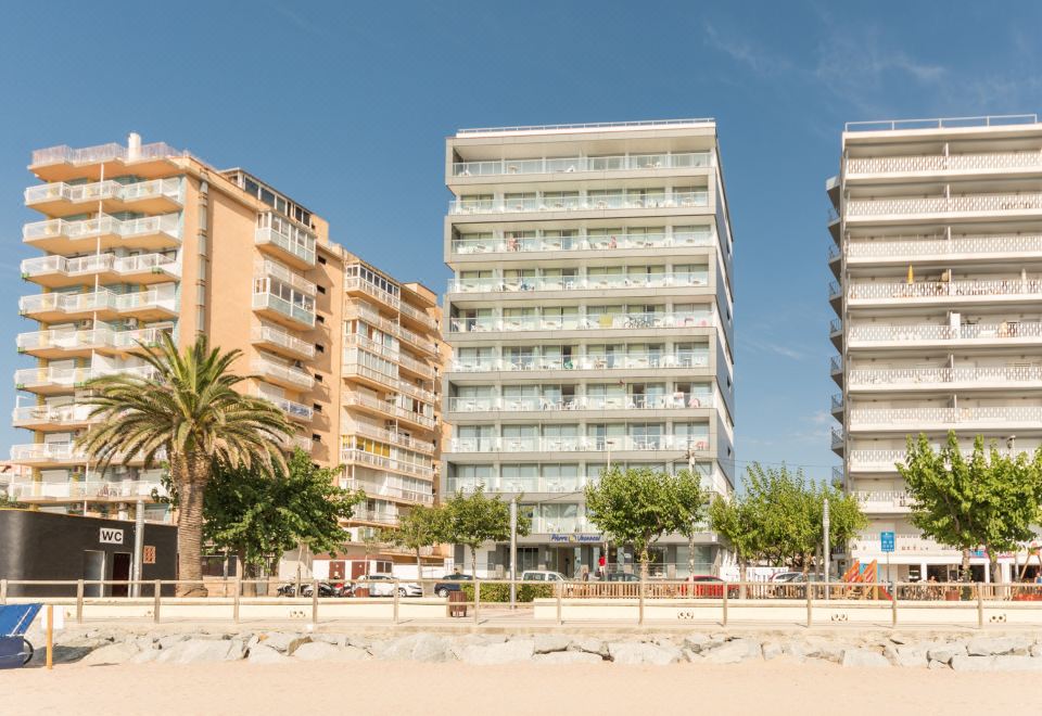 a beachfront apartment building with multiple balconies and palm trees , under a clear blue sky at Pierre & Vacances Blanes Playa