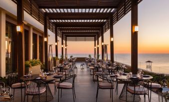 an outdoor dining area with a view of the ocean , featuring tables and chairs under a wooden canopy at Rixos Water World Aktau