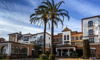 a large building with a courtyard , featuring a palm tree and a clock on the side at Barcelo Isla Canela Hotel