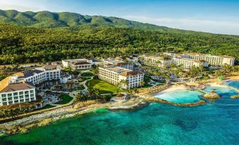 An aerial view displays the resort and the water surrounding it, featuring a vast expanse of green grass at The Ritz-Carlton Golf & Spa Resort, Rose Hall, Jamaica