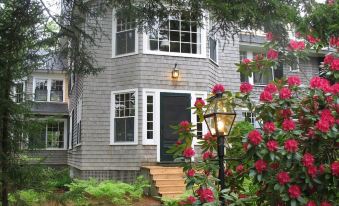 a house with a gray exterior and large windows is surrounded by pink flowers and a wooden deck at Harbourside Inn