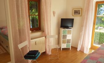 a cozy living room with a window , curtains , and a tv on a shelf , along with a white chair and wooden floor at Martina's Place