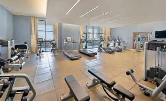 a well - equipped gym with various exercise equipment , including treadmills and stationary bikes , set against a backdrop of large windows at Hilton Suites Makkah