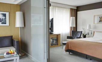a hotel room with a bed , a chair , and a tv . also a bathroom visible in the room at Steigenberger Airport Hotel Amsterdam