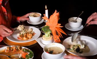 a table with various dishes , including a bowl of soup and a plate of vegetables , has a candle in the center at The Imperial Hotel