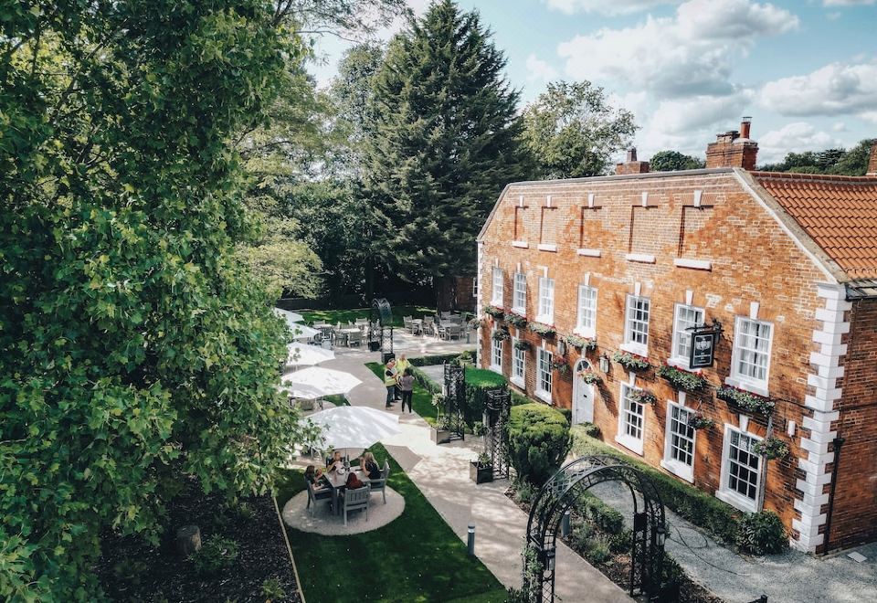 a brick building with a white awning is surrounded by trees and bushes , with an outdoor dining area in the foreground at The Knaresborough Inn - the Inn Collection Group