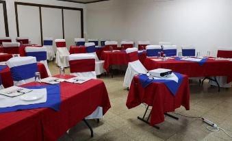 a large , empty conference room with red and blue tablecloths , white chairs , and tables set for meetings or events at Hotel Playa Bonita