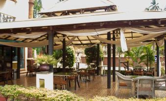 a covered patio with wooden furniture and umbrellas , surrounded by lush greenery and a wooden bench at Sun City Resort