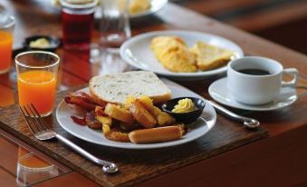 a wooden dining table with a plate of food , including toast , eggs , and sausage , accompanied by a cup of coffee at Oxford Suites Pendleton