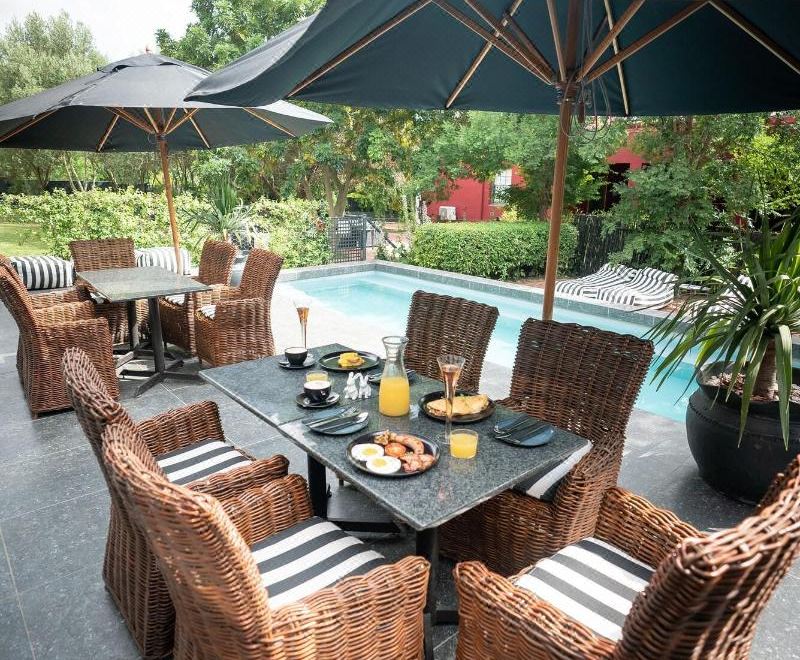 a patio set with a table and chairs , an umbrella , and potted plants overlooking a pool at Ruby Rose