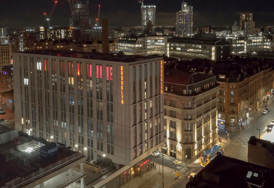 a city street at night , with buildings lit up and cranes visible in the background at voco MANCHESTER - CITY CENTRE