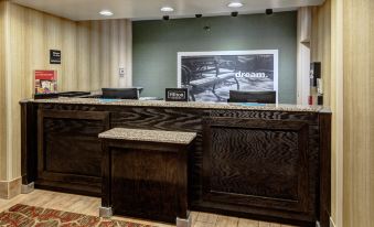 a wooden reception desk with a bench , surrounded by chairs and a poster of the same scene at Hampton Inn Ashland
