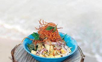 a blue bowl filled with a variety of vegetables and noodles is placed on a wooden table at Pousada Praia Dos Carneiros