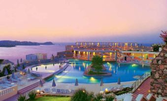 a large resort with a pool and ocean view at sunset , surrounded by lush greenery at Athina Palace Resort & Spa
