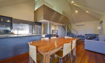 a wooden dining table surrounded by white chairs in a room with hardwood floors and a staircase at Exmouth Escape Resort