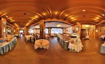 a panoramic view of a large dining room with wooden floors and multiple tables , some of which are covered in white tablecloths at Hotel Villa Argentina