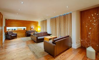 a spacious living room with wooden floors , brown leather couches , and large windows covered by curtains at Hope Street Hotel