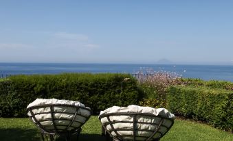 two wicker chairs placed next to each other in a grassy area with a view of the ocean at Hotel Ravesi