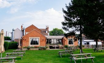 a brick building with a red roof is surrounded by green grass and picnic tables at The Saracens Head