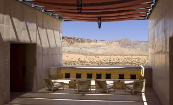 a desert landscape with a building under a large window , and a patio area with several chairs and tables at Amangiri