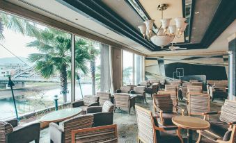 a restaurant with wooden chairs and tables , a chandelier hanging from the ceiling , and palm trees outside at Numazu River Side Hotel
