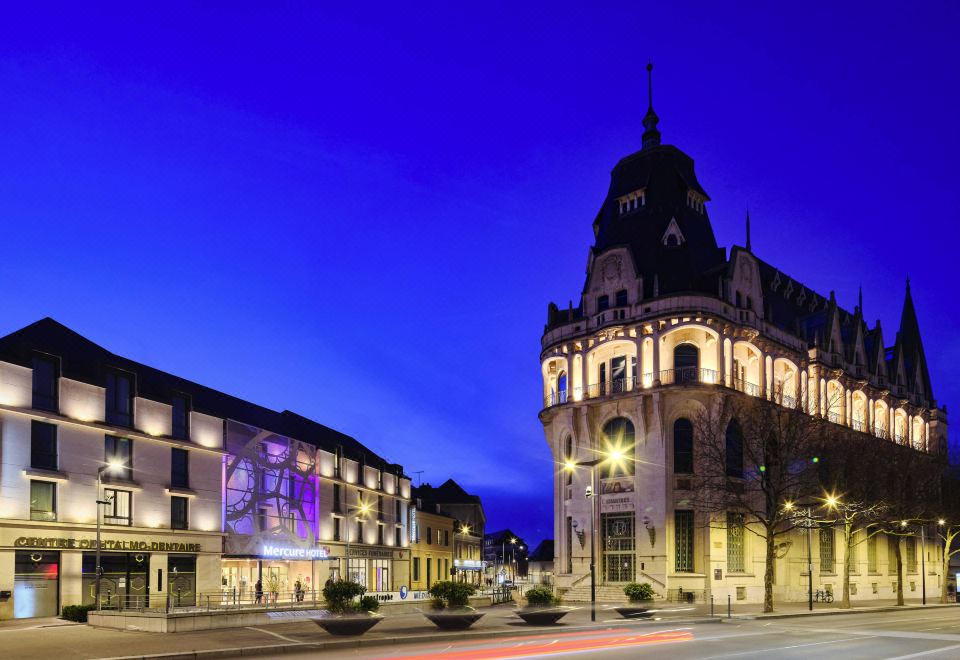 a city street at night , with a large building on the left side of the road and a traffic light in the middle of the street at Mercure Chartres Cathedrale