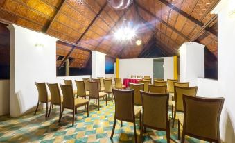 a room with wooden chairs and tables arranged in rows , under a thatched roof with a red fire pit at Over the Hill