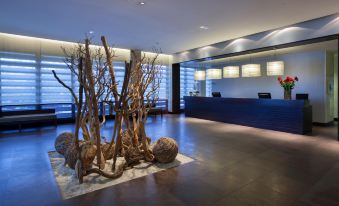 a modern office lobby with a reception desk , large potted plants , and a sculpture of trees at NH Collection Santiago de Compostela