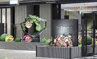 a flower arrangement is displayed on a black and white checkered stand in front of the entrance to the brasserie at Hotel Nikko Kansai Airport