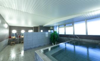 an indoor swimming pool with a blue tiled floor , surrounded by white walls and large windows at Hotel Hokke Club Kumamoto